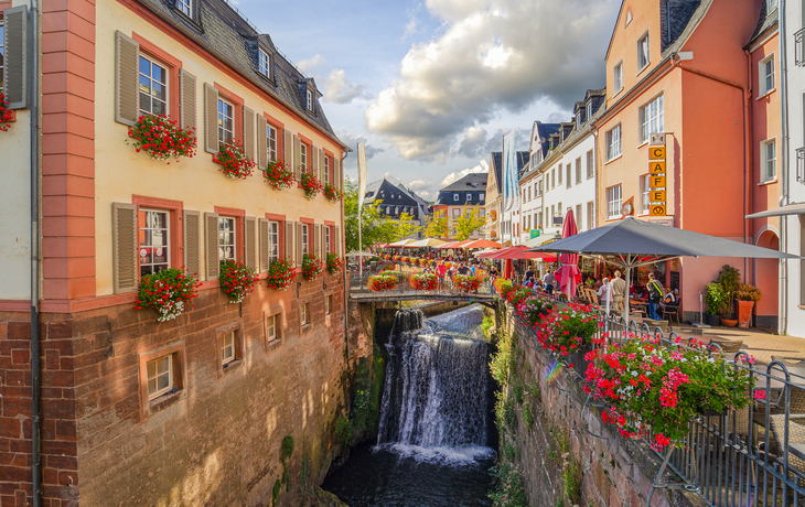 Altstadt-Gasse mit Wasserfall und Blumendekorationen an den Häusern.