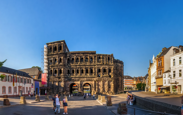Menschen spazieren vor der Porta Nigra in Trier bei klarem Himmel.