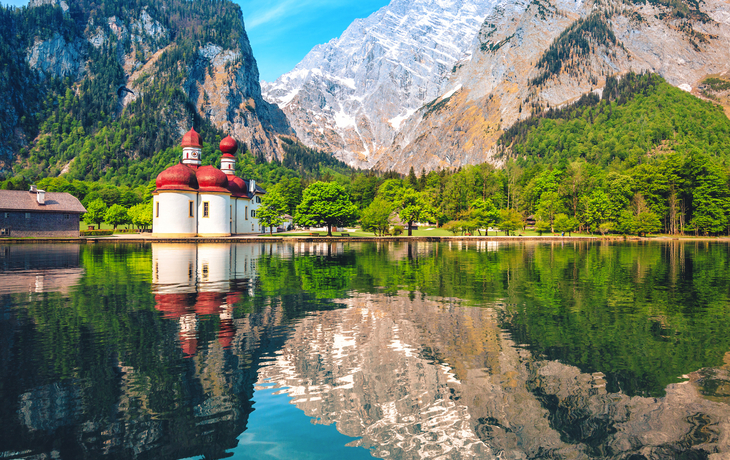 Bergsee mit Kapelle und Bergreflexionen im Wasser.