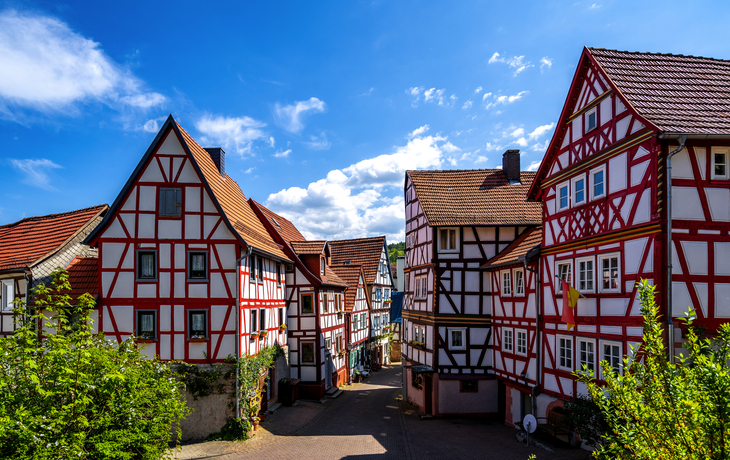 Fachwerkhäuser in einer sonnigen Altstadt mit blauem Himmel im Hintergrund.