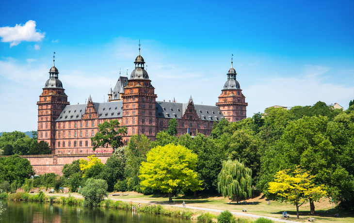 Schloss Johannisburg mit blauem Himmel und grüne Bäume im Vordergrund.