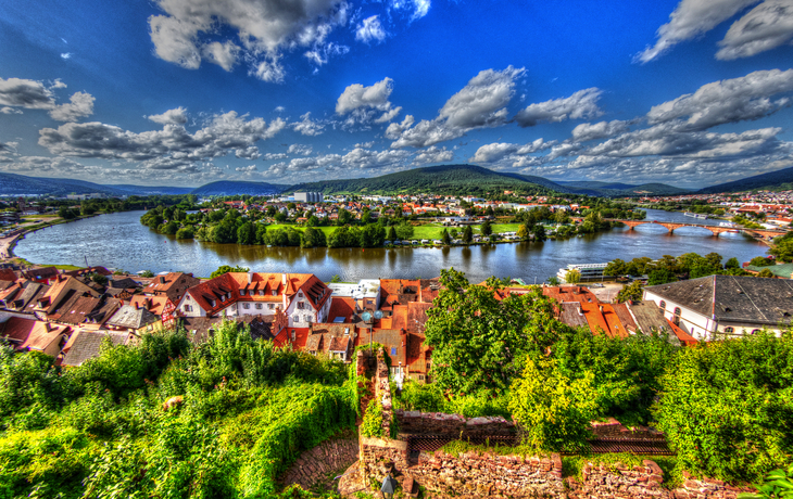 Stadtansicht mit Fluss, grünen Wiesen und blauen Himmel mit Wolken.