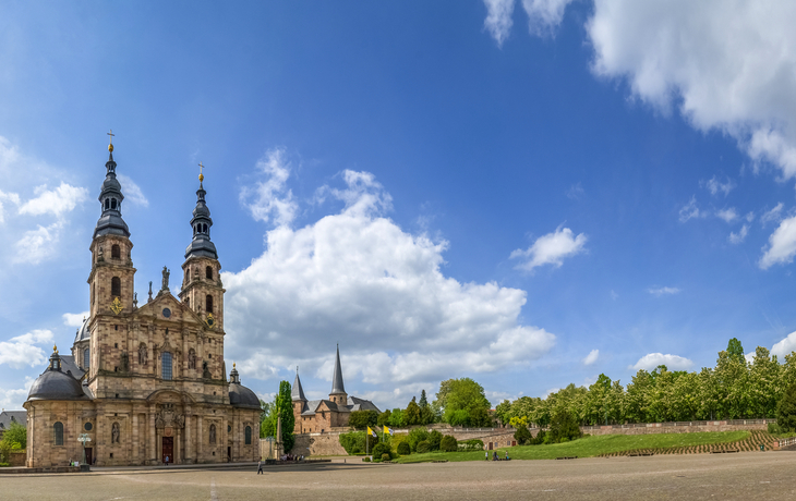 Barocke Fassade einer Kirche mit zwei Türmen unter blauem Himmel.