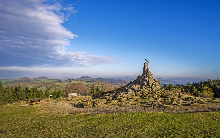 Landschaftspanorama mit Monument auf Hügel unter blauem Himmel.