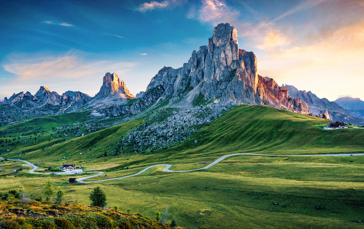 Berglandschaft mit grünem Tal und kurviger Straße bei Sonnenuntergang.