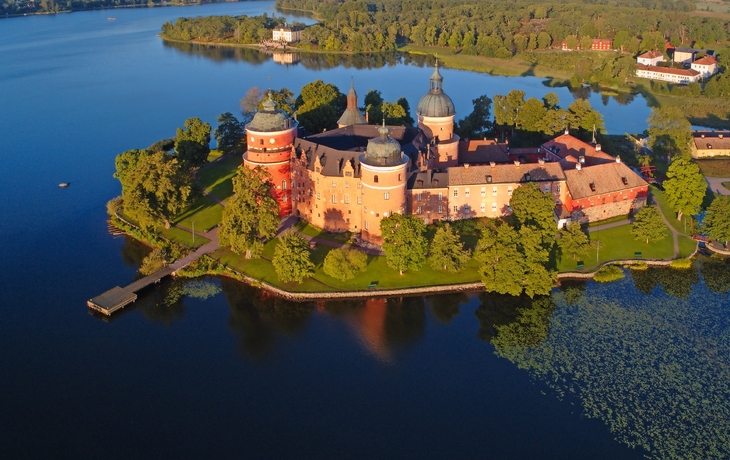 Luftaufnahme einer historischen Burg auf einer Insel in einem See, umgeben von Bäumen.