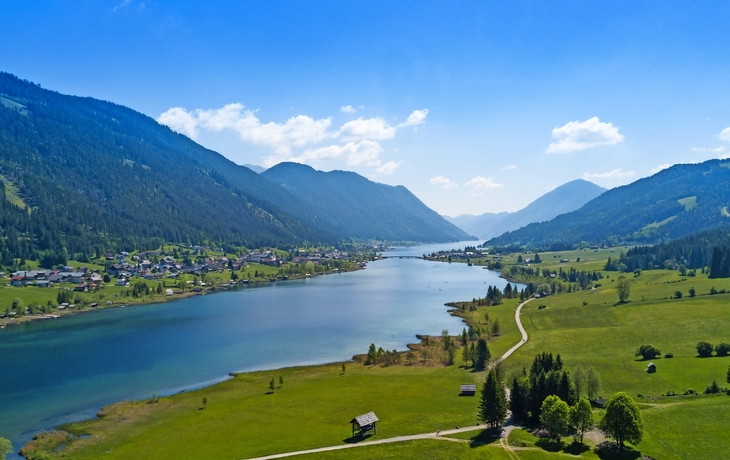 Mountainlandschaft mit See und Dorf im Tal bei klarem Himmel.
