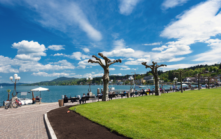 Promenade von Velden am Wörthersee mit Blick auf den See und umliegende Natur bei sonnigem Wetter.