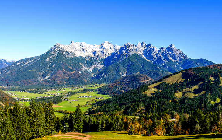 Berglandschaft mit grünen Tälern und schneebedeckten Gipfeln unter klarem, blauem Himmel.