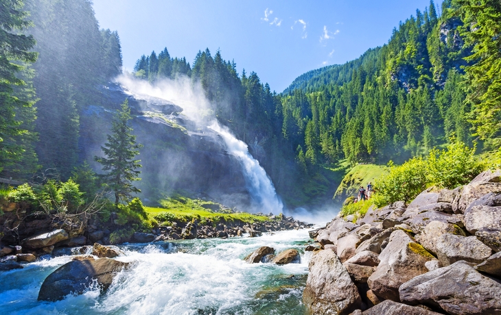 Wasserfall in alpiner Landschaft mit Fluss, Felsen und Bäumen.