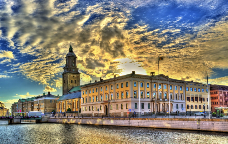 Historisches Gebäude an einem Fluss bei Sonnenuntergang mit dramatischem Himmel.