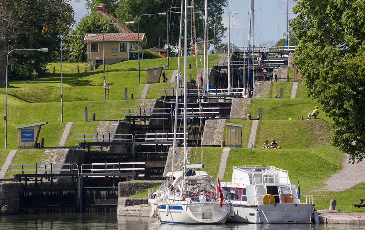 Boote vor einer Schleusentreppe mit grünem Ufer und Spaziergängern.