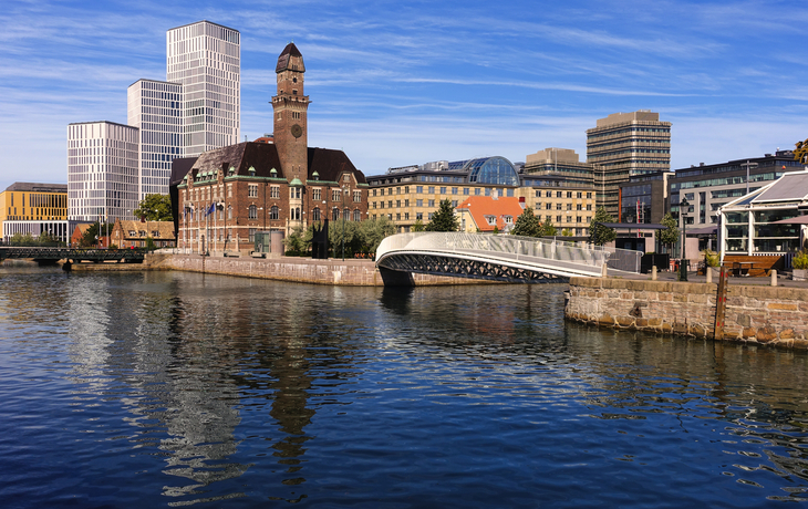 Stadtlandschaft mit historischem Gebäude, modernen Hochhäusern und einer Brücke am Wasser.