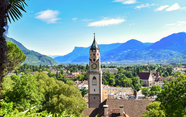 Kirchturm vor Alpenpanorama und Stadt im Tal.