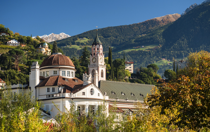 Kirchturm und Gebäude vor Alpenlandschaft im Herbstlicht