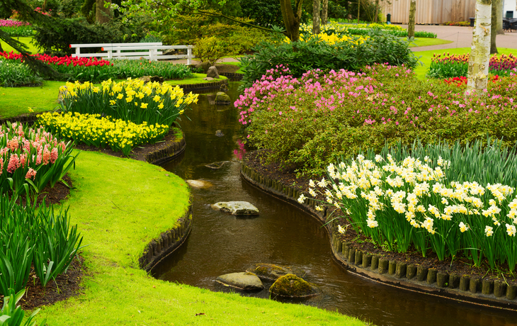 Ein gepflegter Garten mit Blumenbeeten und einem kleinen Bach.