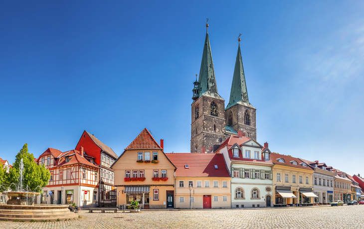 Mittelalterliche Stadtansicht mit Marktplatz und Kirchtürmen unter blauem Himmel.
