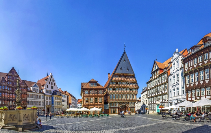 Historischer Marktplatz mit Fachwerkhäusern und Cafés bei klarem Himmel.