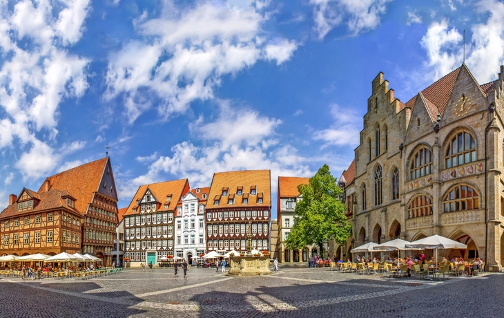 Historischer Marktplatz mit Fachwerkhäusern und Menschen bei sonnigem Wetter.