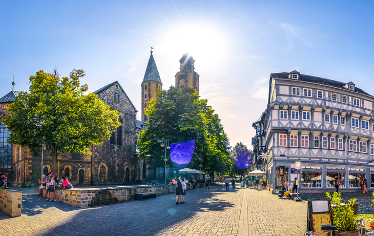 Historische Gebäude und Kirche auf einem sonnigen Platz mit Menschen.