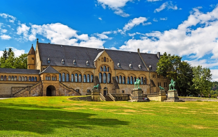 Schloss mit grüner Wiese, blauer Himmel und Wolken im Hintergrund.