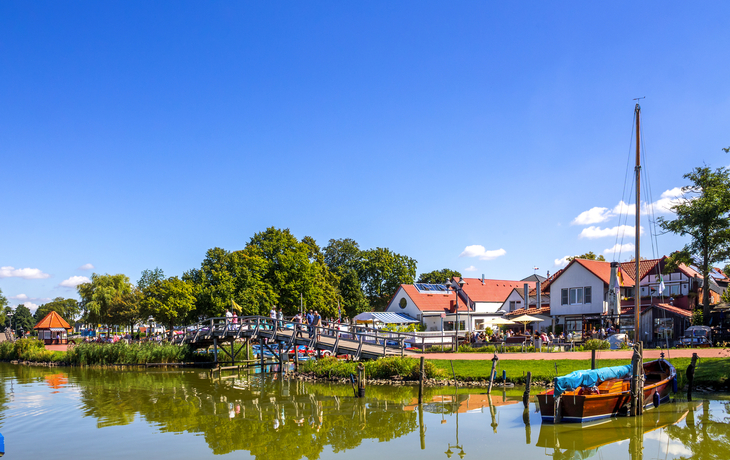 Ein ruhiger Dorfhafen mit Booten, Brücke und Häusern am Wasser.