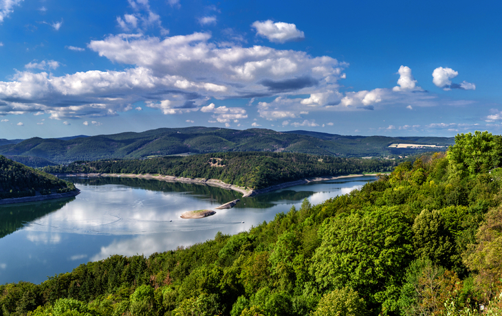 Panorama einer Flusslandschaft mit bewaldeten Hügeln und einem Schloss.