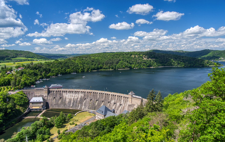 Staumauer einer Talsperre mit umliegender Landschaft und blauem Himmel