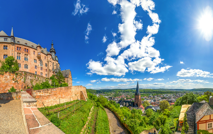 Panorama einer Burg über einer Stadt bei klarem Himmel mit einigen Wolken.