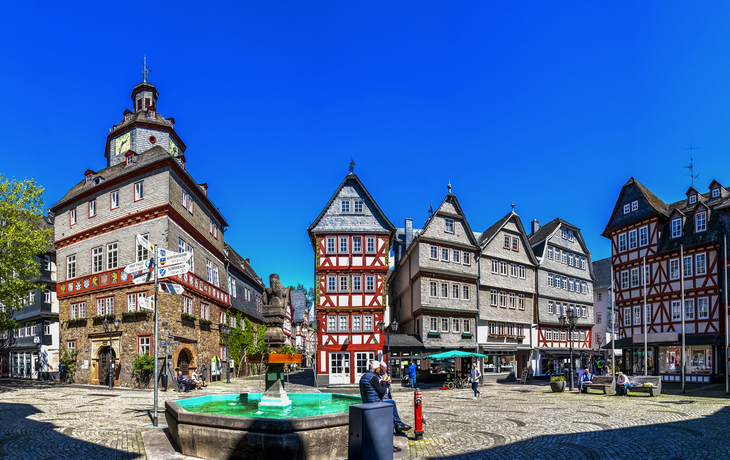 Panorama eines historischen Fachwerkplatzes mit Brunnen bei klarem Himmel.