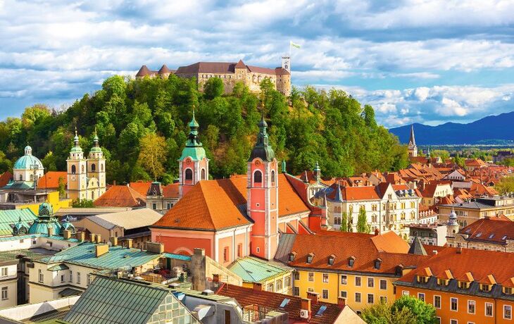 Blick auf Ljubljana mit Burg auf Hügel und bunten Häusern im Vordergrund.