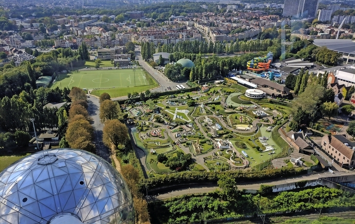 Blick von oben auf einen Park mit Miniaturgebäuden und umliegender Stadtlandschaft.