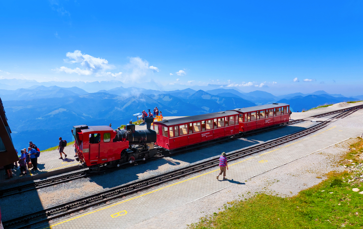 Rote Zahnradbahn auf Bergstation mit Blick auf die Alpen.