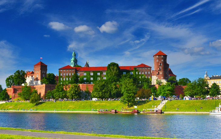 Panorama des Wawel-Schlosses in Krakau, mit blauem Himmel und Fluss im Vordergrund.