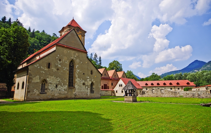 Historisches Kloster mit rotem Dach in grüner Landschaft unter blauem Himmel.