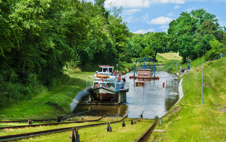 Ein Boot passiert eine Schiffshebewerkanlage in einer grünen Landschaft.