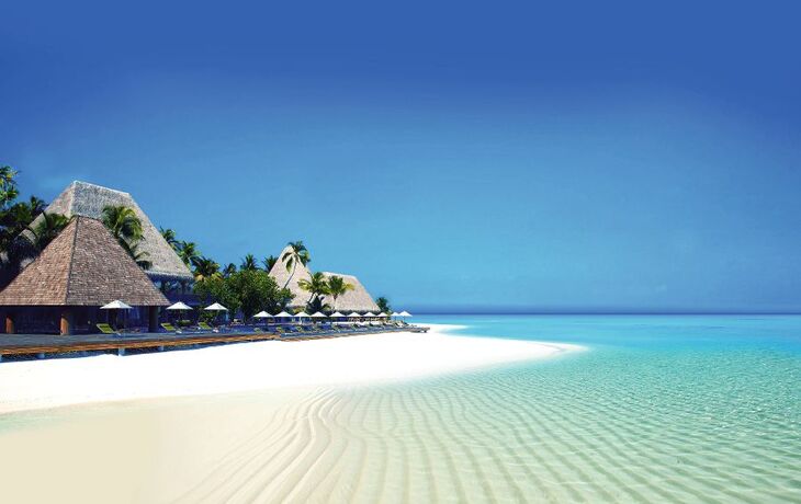 Strand mit Palmen und strohgedeckten Hütten am klaren, blauen Meer.
