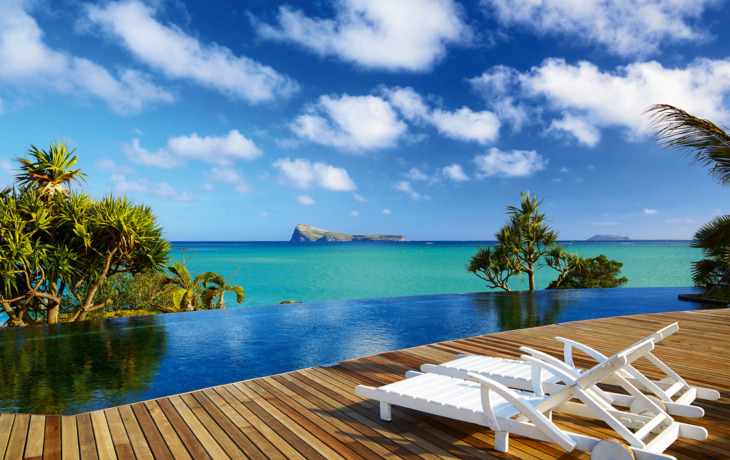 Zwei weiße Liegestühle auf einer Holzterrasse am Infinity-Pool mit Meerblick.