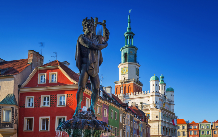 Statue eines Mannes mit Lyra vor bunten Gebäuden und einem Turm.