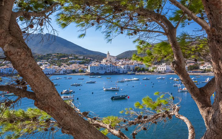 Blick auf eine Küstenstadt mit Kirche, umrahmt von Bäumen, Boote im Vordergrund.