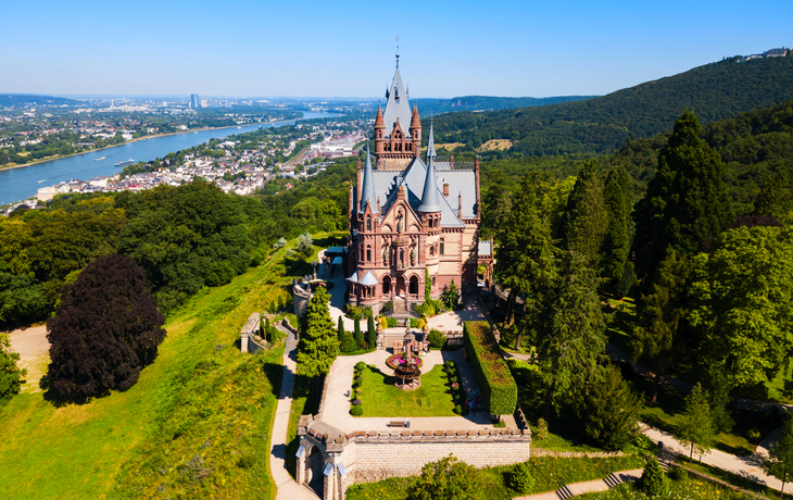 Luftaufnahme von Schloss Drachenburg umgeben von Grün mit Blick auf den Rhein.