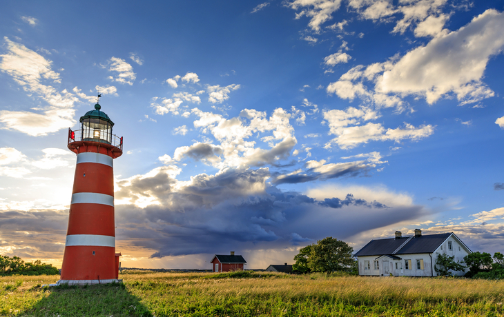 Leuchtturm und Haus in einer grünen Landschaft bei Sonnenuntergang.