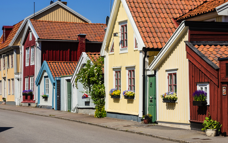 Reihe von bunten skandinavischen Holzhäusern mit Blumen an den Fenstern unter blauem Himmel.
