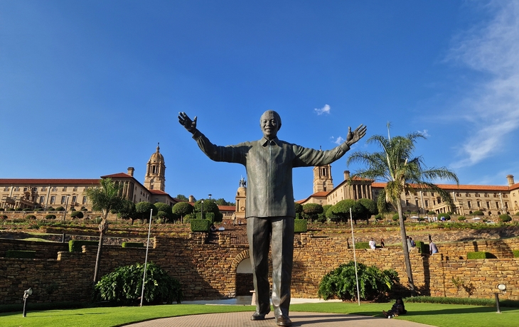 Statue eines Mannes mit ausgestreckten Armen vor einem historischen Gebäude.