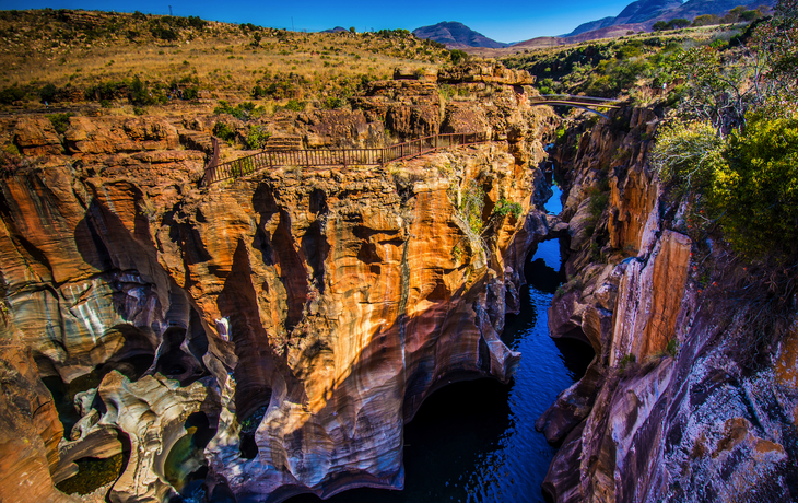 Farbenfrohe Felsformationen und Fluss in einer Schlucht bei sonnigem Wetter.