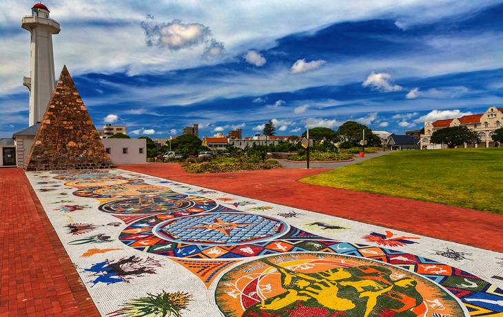 Bunt gestalteter Platz mit einem Leuchtturm und Pyramidenstruktur im Hintergrund.