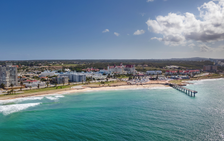 Küstenlinie mit Strand, Stadtgebäuden und einem langen Steg im Ozean.