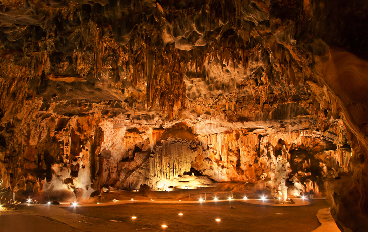 Beleuchtete Höhle mit Stalagmiten und Stalaktiten.