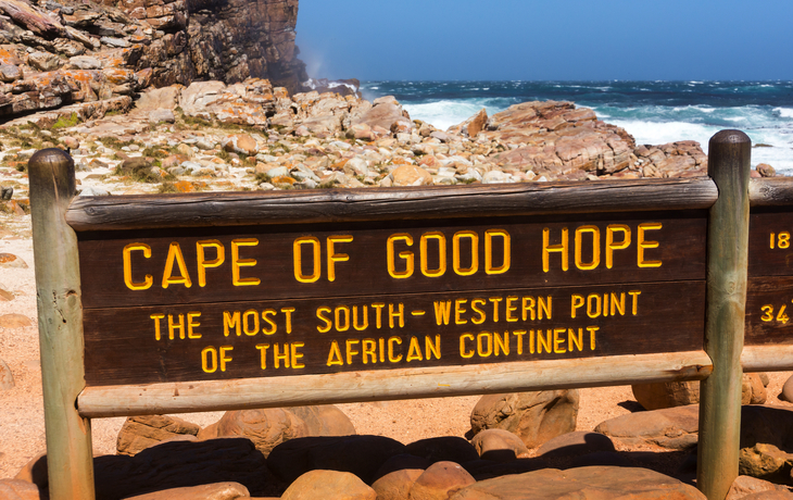 Holzschild am Kap der Guten Hoffnung vor Felsenküste und Meer.