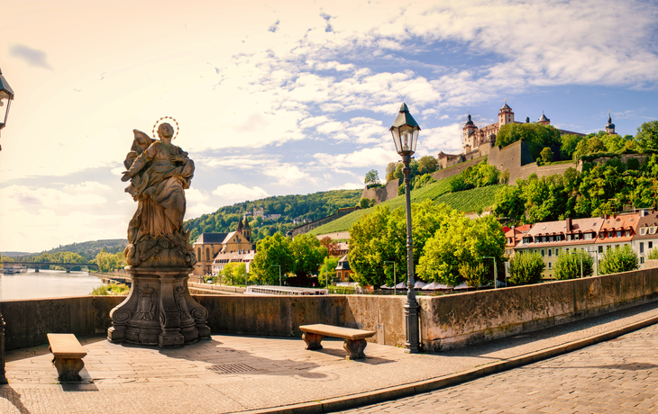 Statue auf einer Brücke mit Blick auf eine befestigte Burg und Hügel im Hintergrund.